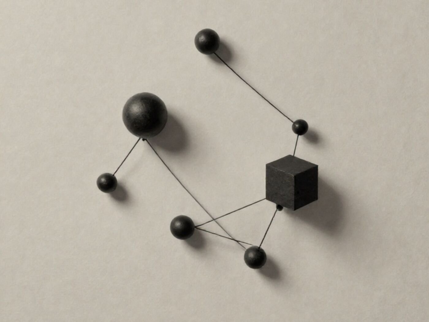 Small spheres and one cube arranged in a constellation and joined by taut black thread