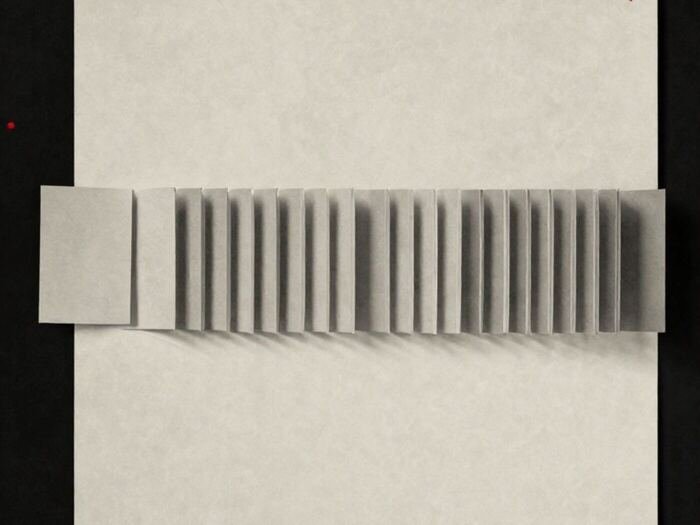 A row of identical paper cards lying flat, with one lifted and standing on its edge
